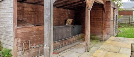 A wooden shed with a bench inside, a door, and a stone pathway leading to it.
