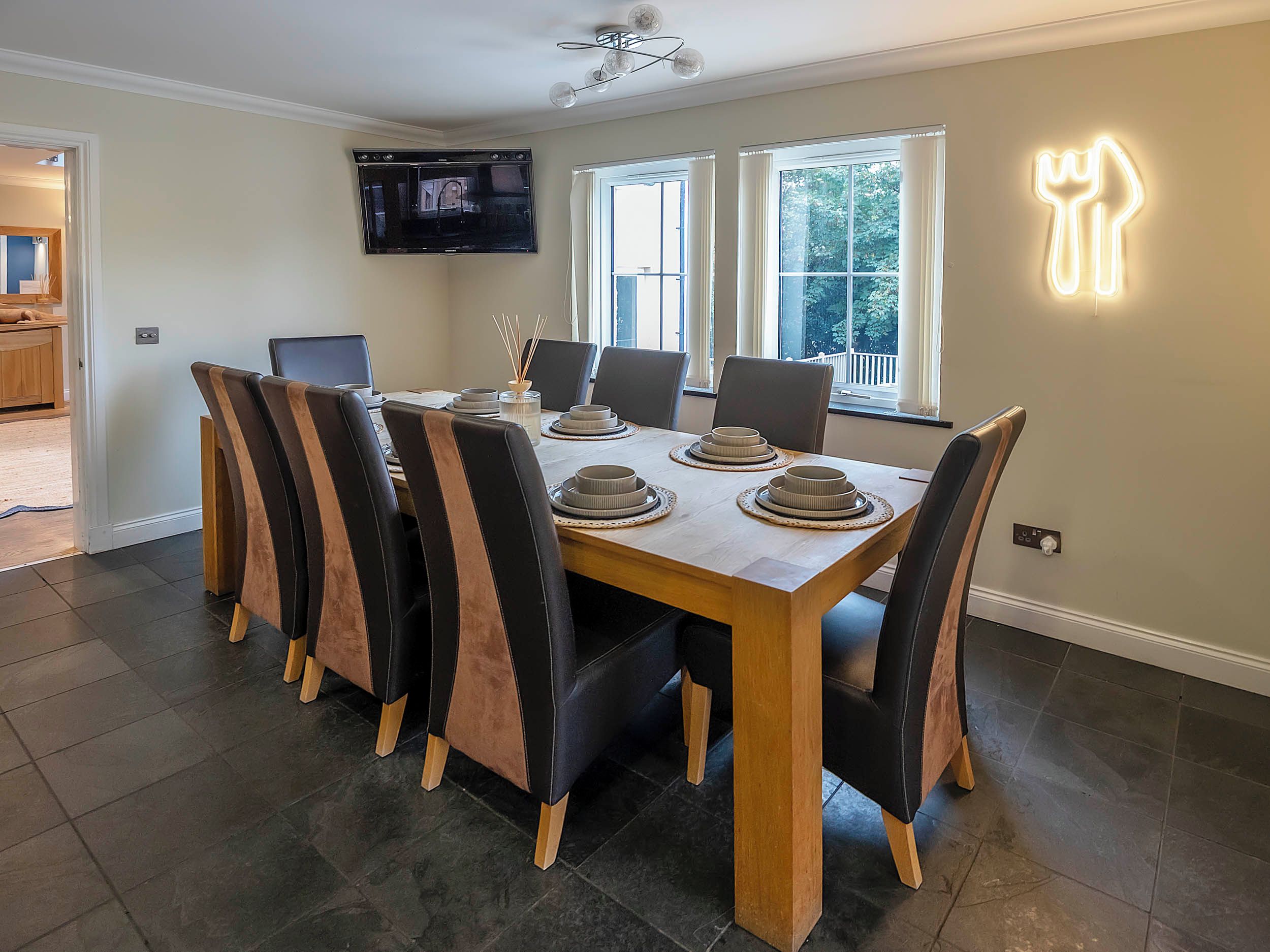 Un comedor con una mesa de madera, seis sillas y un televisor de pantalla plana montado en la pared.
