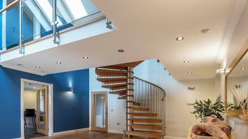 Een modern interieur met een houten spiltrap, een hoog plafond met dakramen en een grote spiegel die de ruimte weerspiegelt.