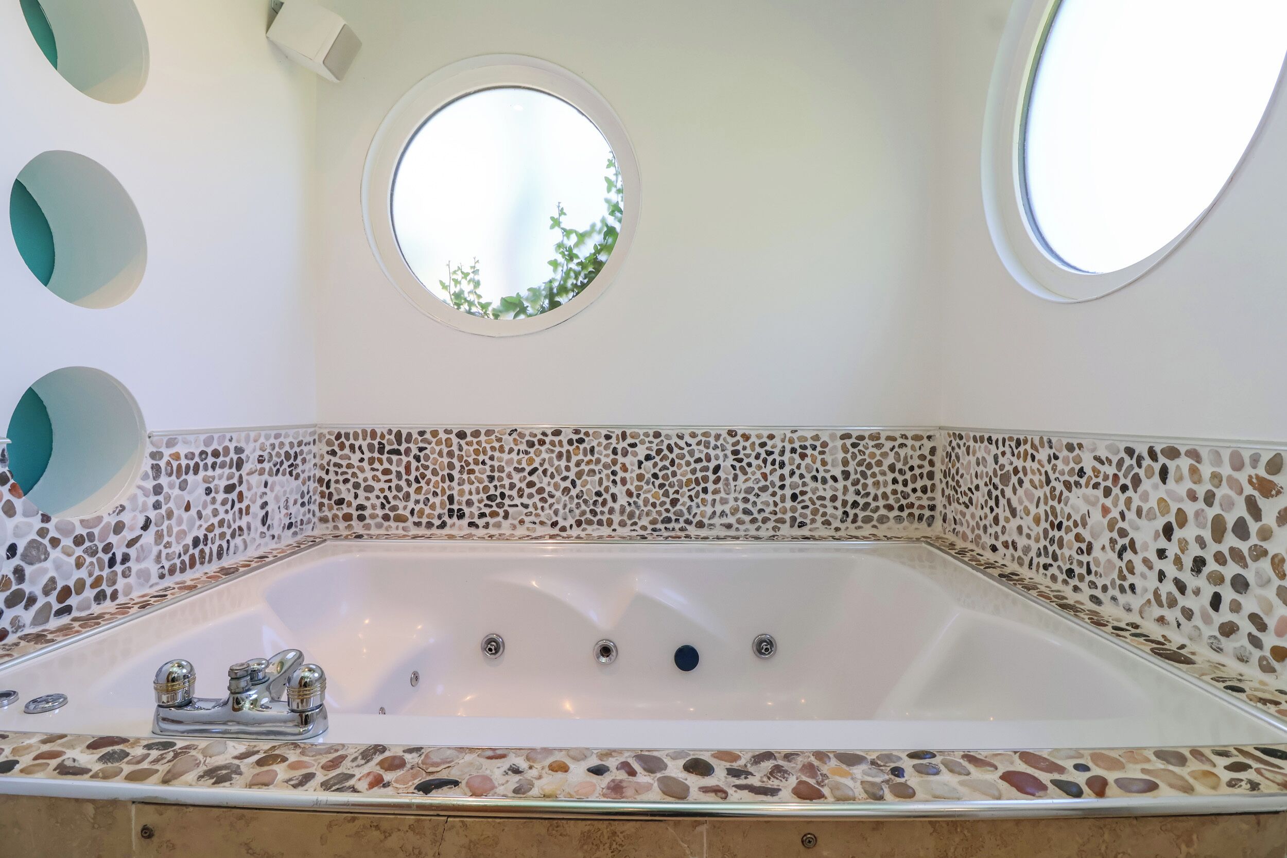 Ein modernes Badezimmer mit freistehender Badewanne, Kiesel-Mosaikfliesen und drei Rundfenstern.