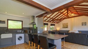 A modern kitchen with a built-in washing machine, a large island with bar stools, and a seating area with a sofa and a table. - Bay Tree Lodge 35 (Ilfracombe)