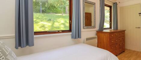 A bedroom with a single bed, a dresser, a mirror, and a window with curtains.