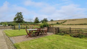 A patio with a table and chairs, surrounded by a grassy lawn and a brick wall. - The Stables at Daldorch (Mauchline)
