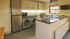 A compact kitchen with a built-in washer and dryer, a gas stove, and a large island with a sink. - The Stables at Daldorch (Mauchline)