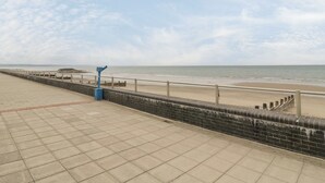 Ein gepflasterter Weg am Strand mit Geländer und einem blauen Teleskop.