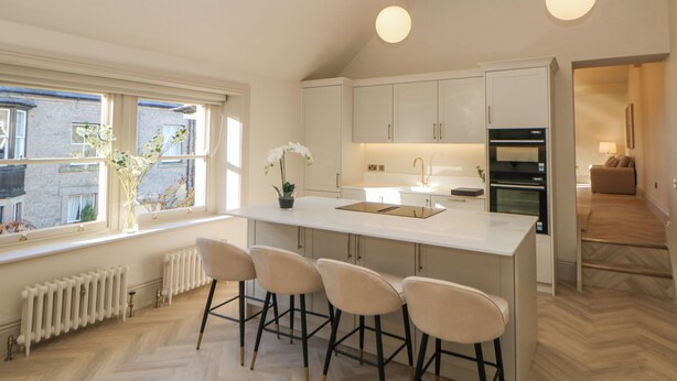 A modern kitchen with a central island, bar stools, a window with a view, and pendant lighting. - Castleton Suite (Buxton)