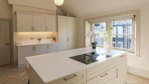 A modern kitchen with white cabinetry, a large island with a sink, and a window with a view of buildings. - Castleton Suite (Buxton)