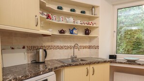 A kitchen with a built-in dishwasher, a sink, and a window with a view of greenery. - Flat 2 Beechcroft (Dartmouth)
