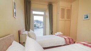 A hotel room with two beds, a window with curtains, a view of a hillside, and a wardrobe. - Flat 2 Beechcroft (Dartmouth)