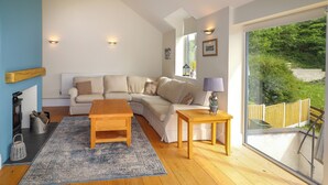 A modern living room with a sofa, a coffee table, and a side table. There is a fireplace, a window with a view of greenery, and a wooden floor. - Bryn Golau (Llangollen)