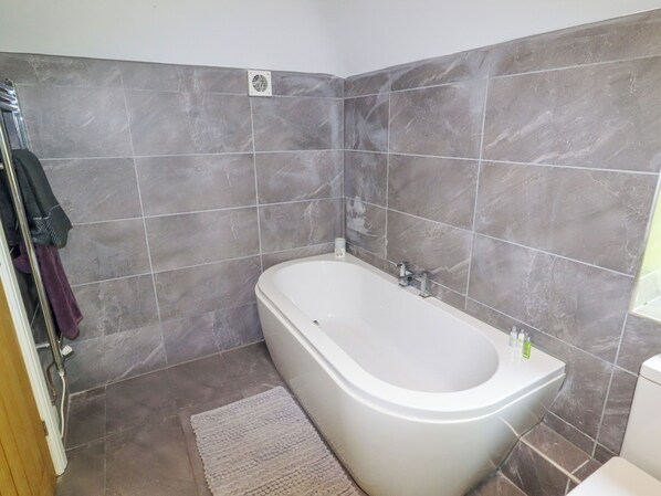 A bathroom with a bathtub, grey tiles, a white sink, and a small rug.