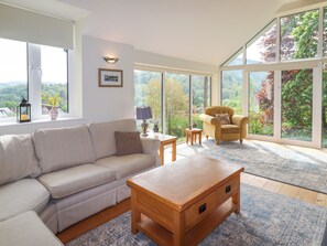 A spacious living room with a large window offering a scenic view, a beige sofa, a wooden coffee table, and a yellow armchair.