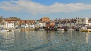 A harbor with boats docked, buildings along the waterfront, and a clear sky. - Melanie's Cottage (Weymouth)