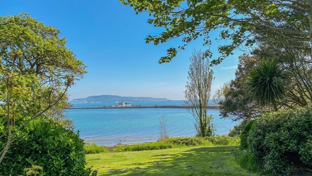 A grassy area with a view of a calm body of water and distant land. - Melanie's Cottage (Weymouth)