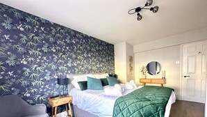 A bedroom with a bed, a chair, a bedside table, a mirror, and a door. - Melanie's Cottage (Weymouth)