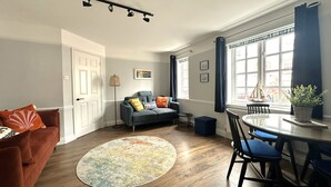 A modern living room with a sofa, a dining table with chairs, a round rug, and a potted plant. - Melanie's Cottage (Weymouth)
