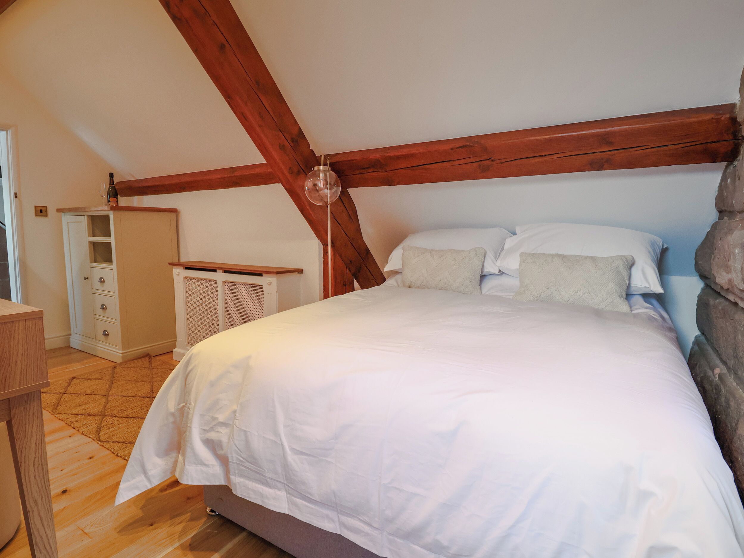 A bedroom with a wooden ceiling, a bed with white bedding, a bedside table, and a wardrobe.