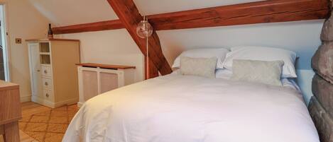 A bedroom with a wooden ceiling, a bed with white bedding, a bedside table, and a wardrobe.