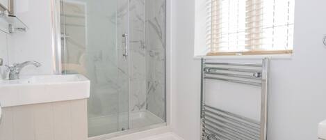 Et moderne badeværelse med et glasvæg-afskærmet brusebad, en hvid vask og et toilet.