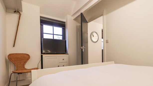 A bedroom with a bed, a dresser, a chair, a window, and a door. - Bee Cottage (Canterbury)