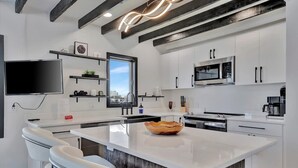Una cocina moderna con armarios blancos, una isla grande, un televisor de pantalla plana y vistas de la ciudad.
