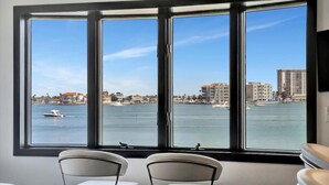 Habitación con un amplio ventanal que da a una masa de agua y al paisaje urbano. Dos sillas blancas están en primer plano.