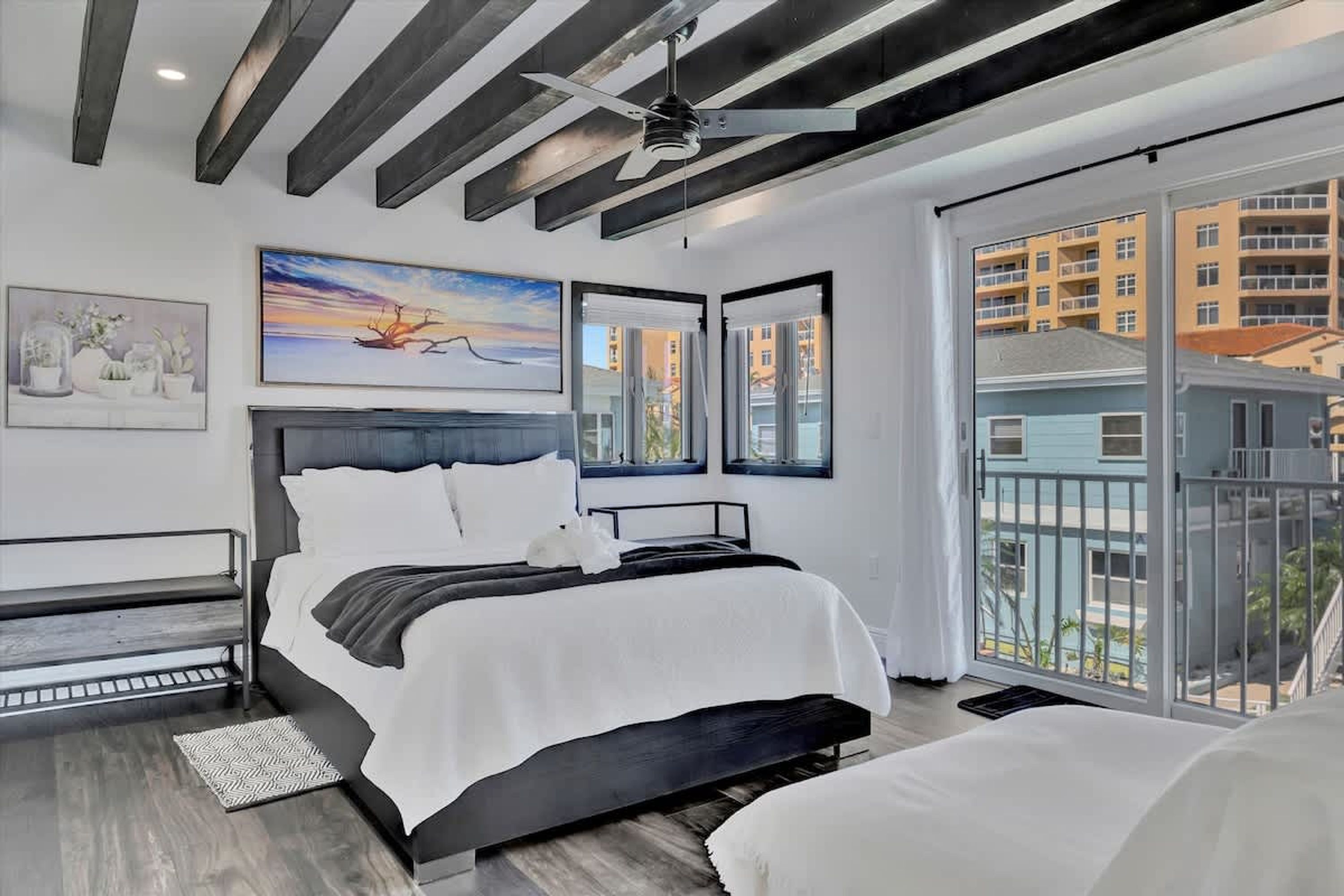 Un dormitorio moderno con una cama grande, un ventilador de techo y amplios ventanales con vistas a la ciudad.
