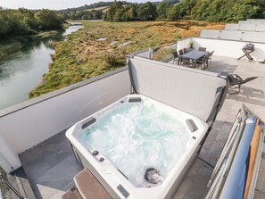 Eine Dachterrasse mit Whirlpool, Sitzgelegenheiten im Freien und Blick auf einen Fluss.