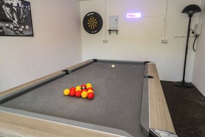 A pool table with balls, a dartboard, and a lamp.