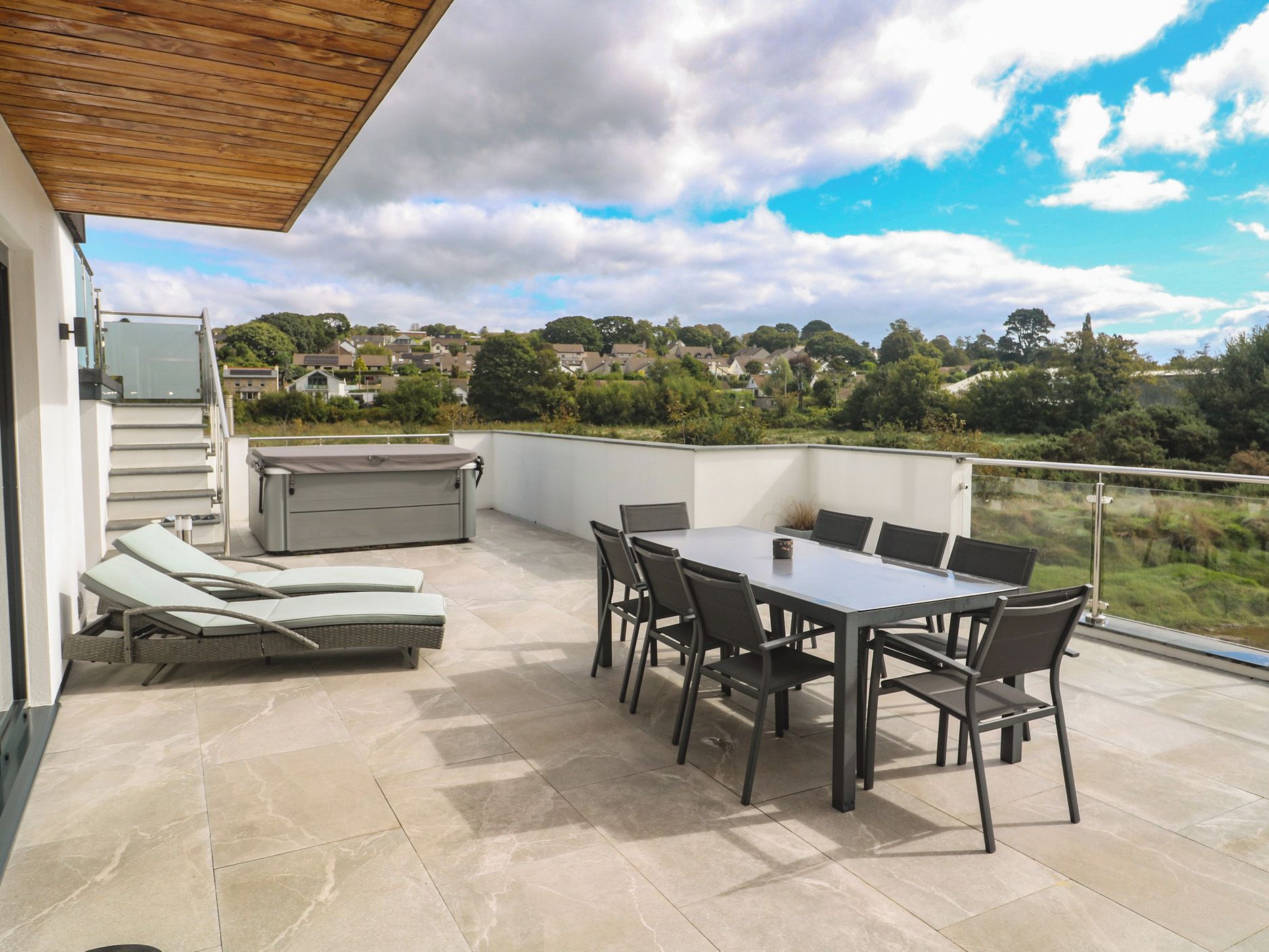 A covered outdoor patio with a table and chairs, a barbecue grill, and a pair of sun loungers.