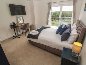 A bedroom with a bed, a desk, a chair, a TV, and a window with a view. - Carnon Gwel, Devoran (Truro)