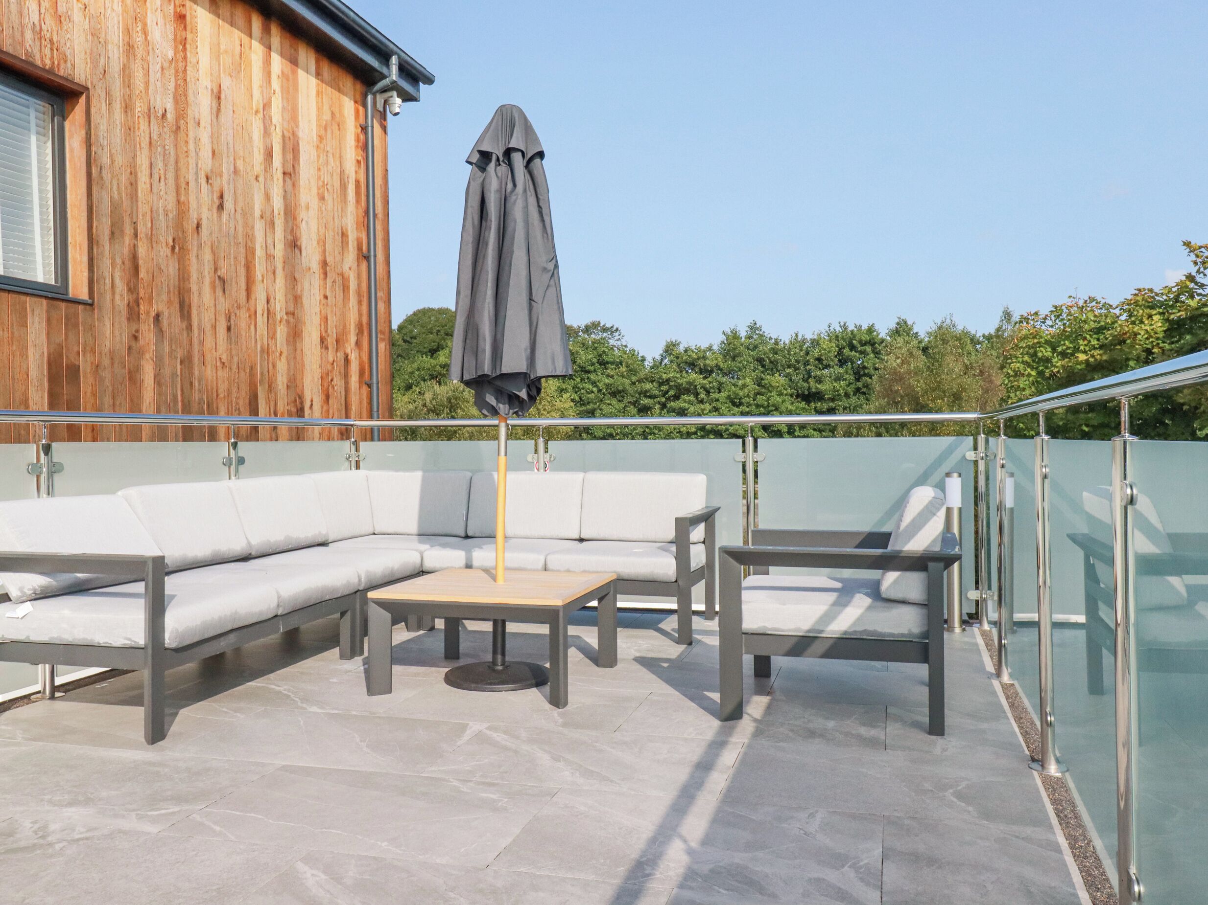 A rooftop terrace with a wooden building, a gray umbrella, a white sofa, and a small table.