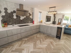 Une cuisine moderne avec un parquet en bois disposé en chevrons, un four encastré et un grand îlot central doté d’un évier.