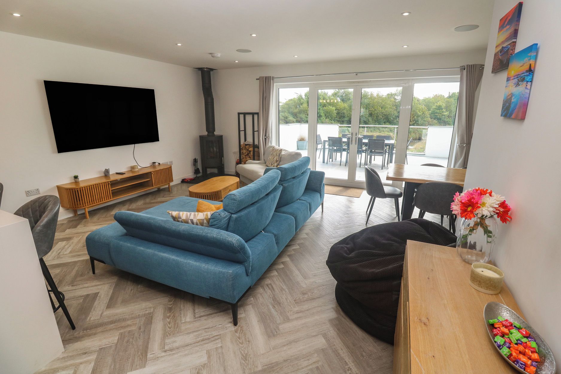 A modern living room with a blue sofa, a black bean bag, a wooden coffee table, and a flat-screen TV mounted on the wall.