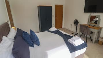 Una habitación de hotel con una cama grande, un escritorio con silla, un televisor y un armario.