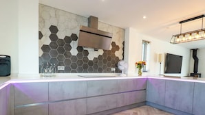 A modern kitchen with a herringbone wood floor, a hexagonal tile backsplash, and a built-in island with a light under-cabinet illumination. - Carnon Gwel, Devoran (Truro)