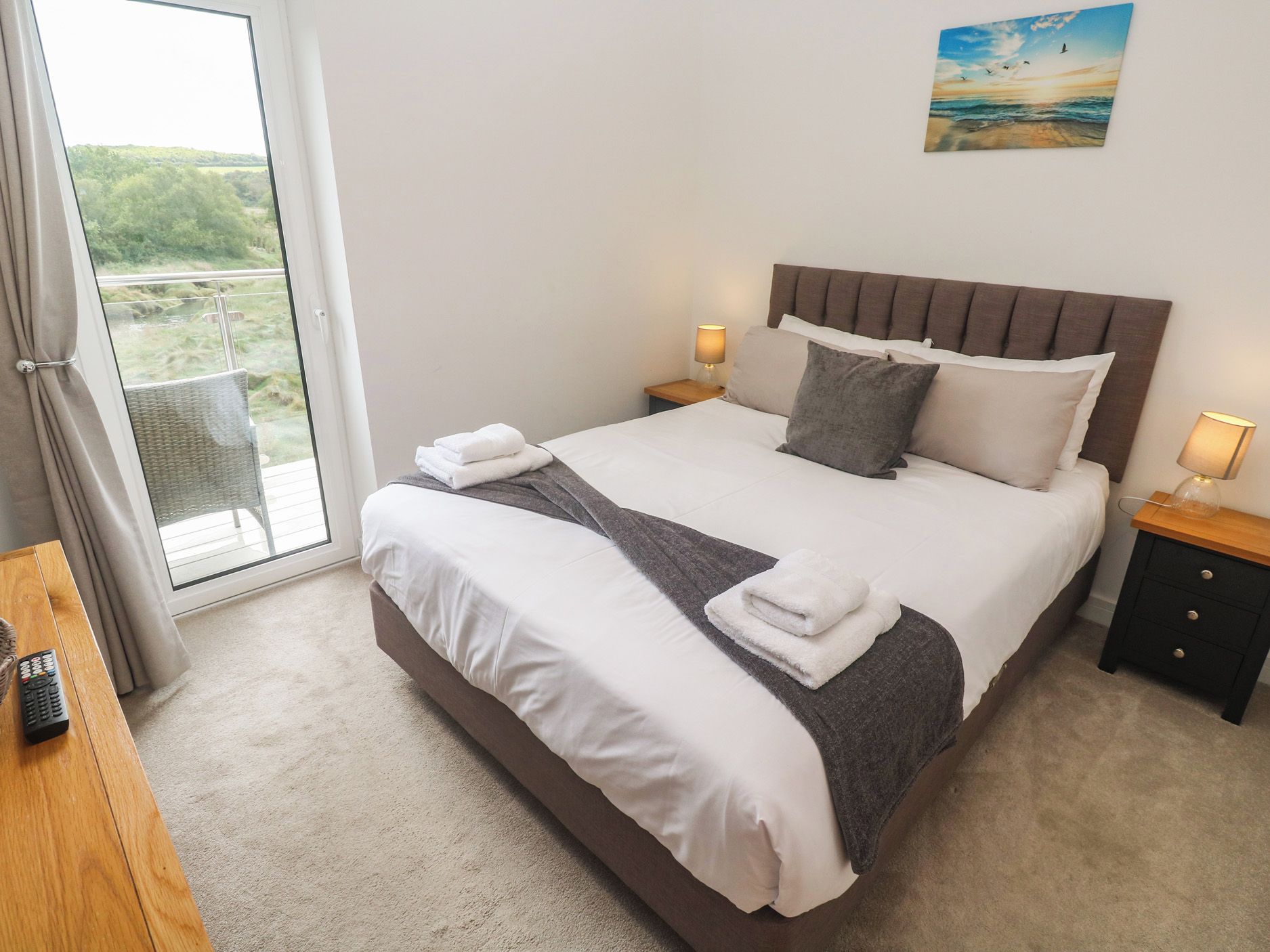 Habitación de hotel con una cama grande, dos mesitas de noche con lámparas, vistas al exterior por una ventana y un cuadro en la pared.