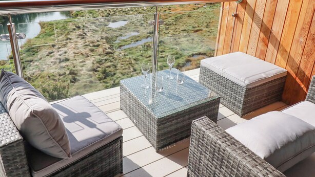 A balcony with wicker furniture, a glass table, and a view of a river and greenery. - Carnon Gwel, Devoran (Truro)