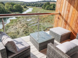 A balcony with wicker furniture, a glass table, and a view of a river and greenery. - Carnon Gwel, Devoran (Truro)
