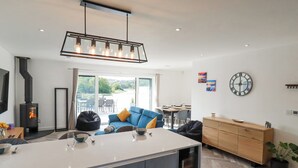 A modern kitchen with a central island, a dining area with a table and chairs, a sofa, and a large window with a view. - Carnon Gwel, Devoran (Truro)