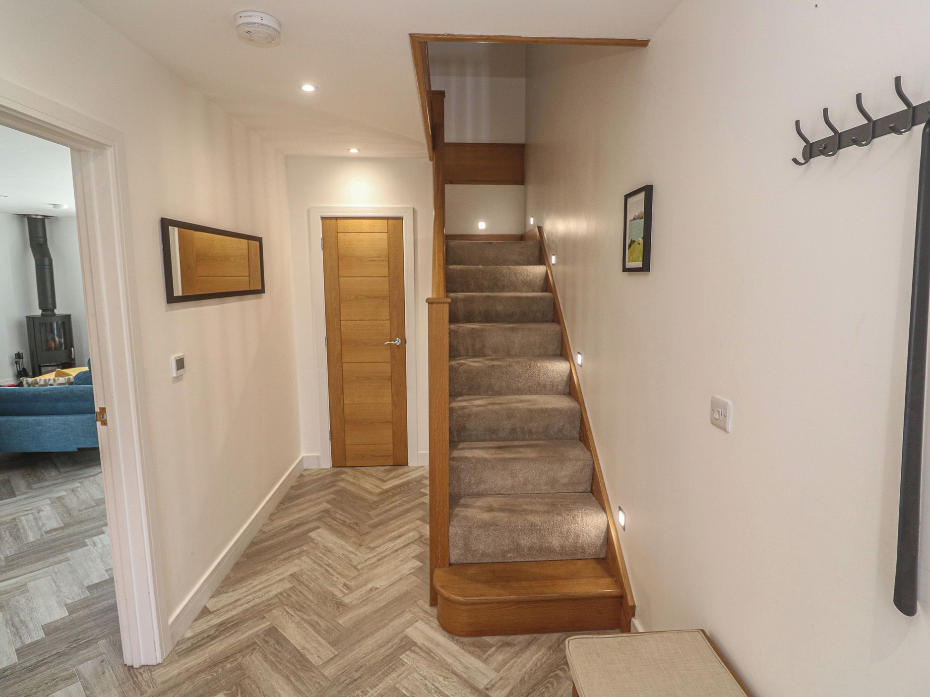 A hallway with a wooden staircase, a door, a coat rack, and a herringbone-patterned floor.