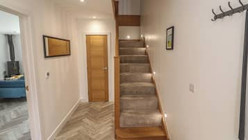 A hallway with a wooden staircase, a door, a coat rack, and a herringbone-patterned floor.