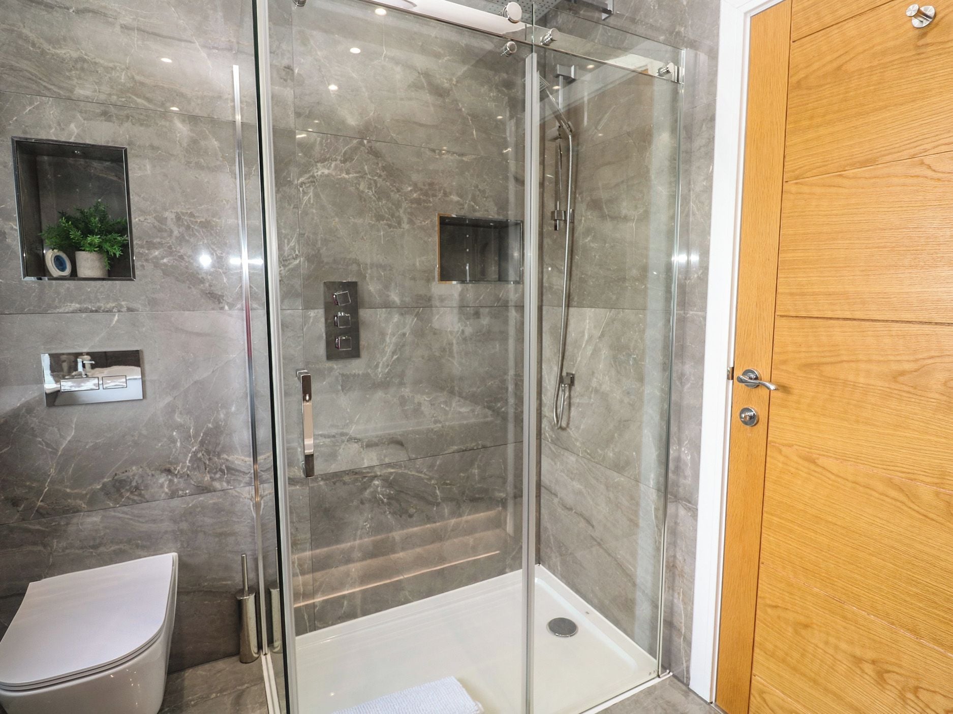 Un baño moderno con ducha envuelta en vidrio, inodoro y puerta de madera.