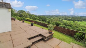 A patio with stone steps leading to a white building, surrounded by a wooden fence and lush greenery. - Addyfield Farmhouse (Windermere)