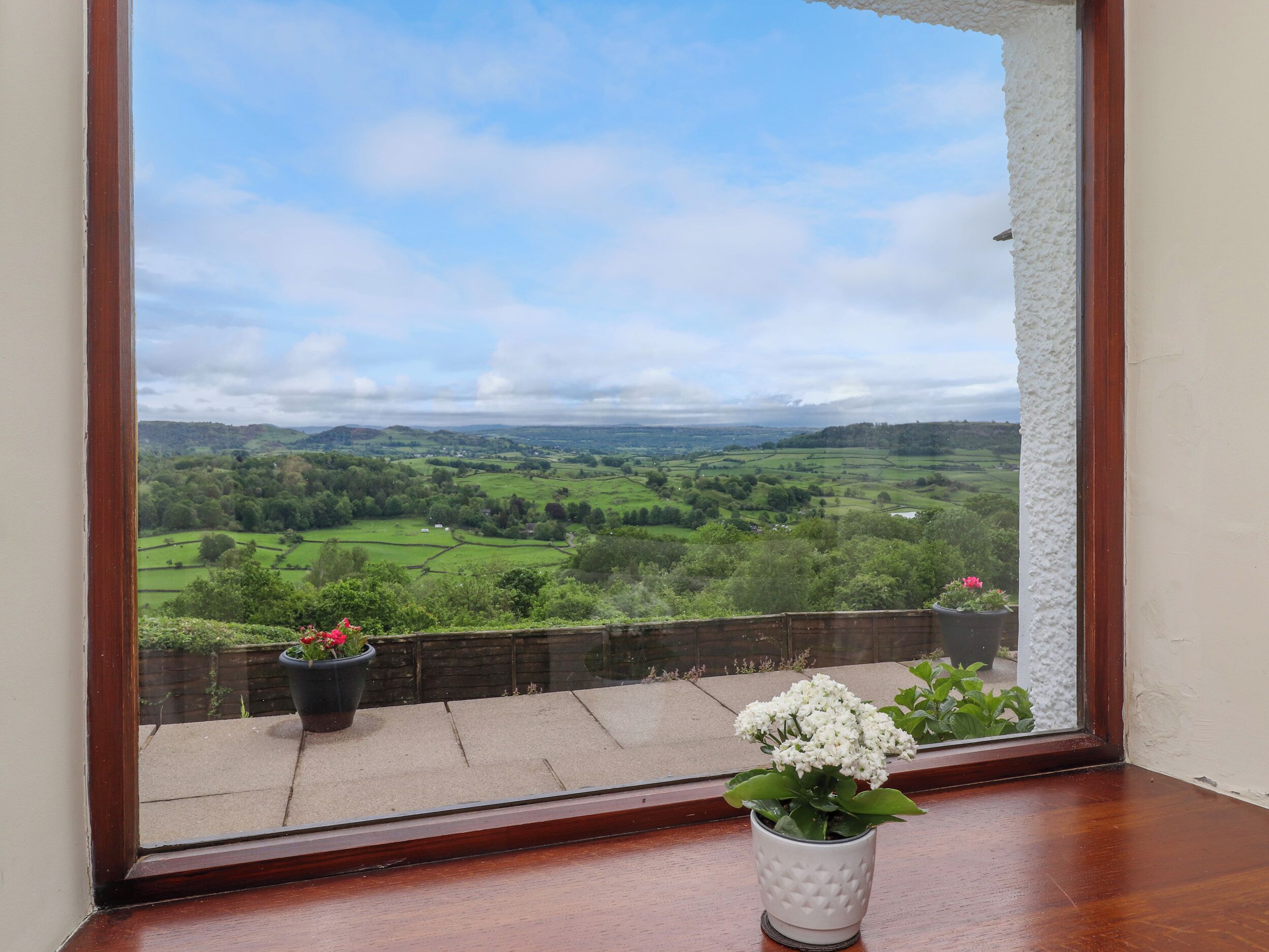 A view from a window overlooking a green landscape with fields and distant hills.