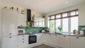 A modern kitchen with white cabinets, a microwave, an oven, and a window with blinds. - Cherry Tree Cottage (Chesterfield)
