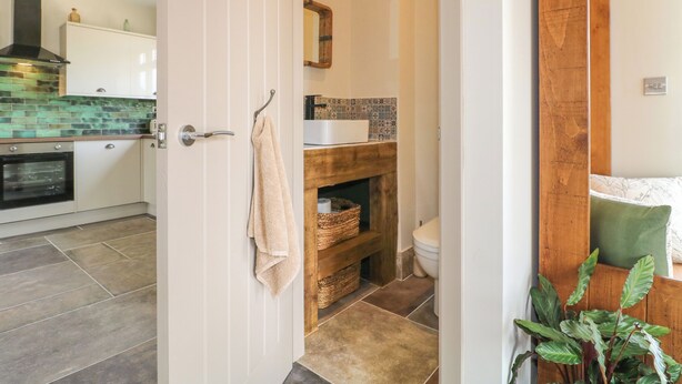 A kitchen with a tiled backsplash, a wooden shelf, and a hanging towel. - Cherry Tree Cottage (Chesterfield)