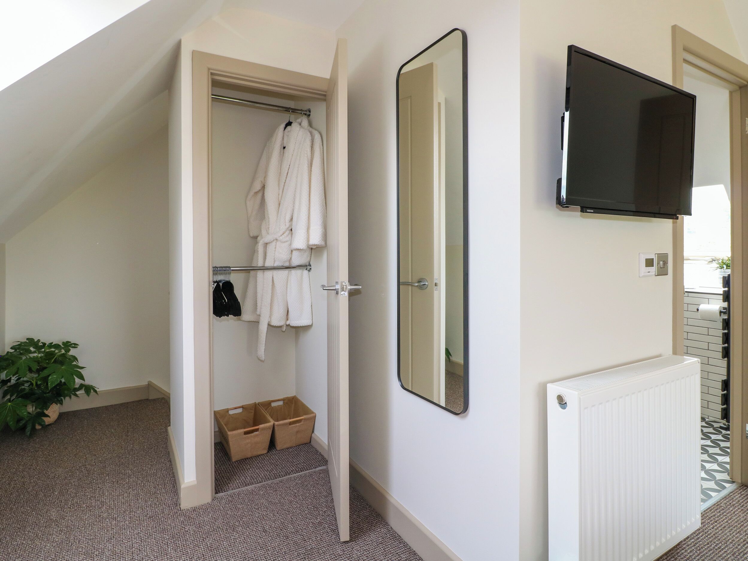 Ein modernes Badezimmer mit Dusche, Handtuchhalter mit Bademantel, großem Spiegel und einem an der Wand montierten Fernseher.