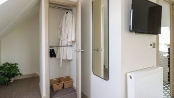 Ein modernes Badezimmer mit Dusche, Handtuchhalter mit Bademantel, großem Spiegel und einem an der Wand montierten Fernseher.