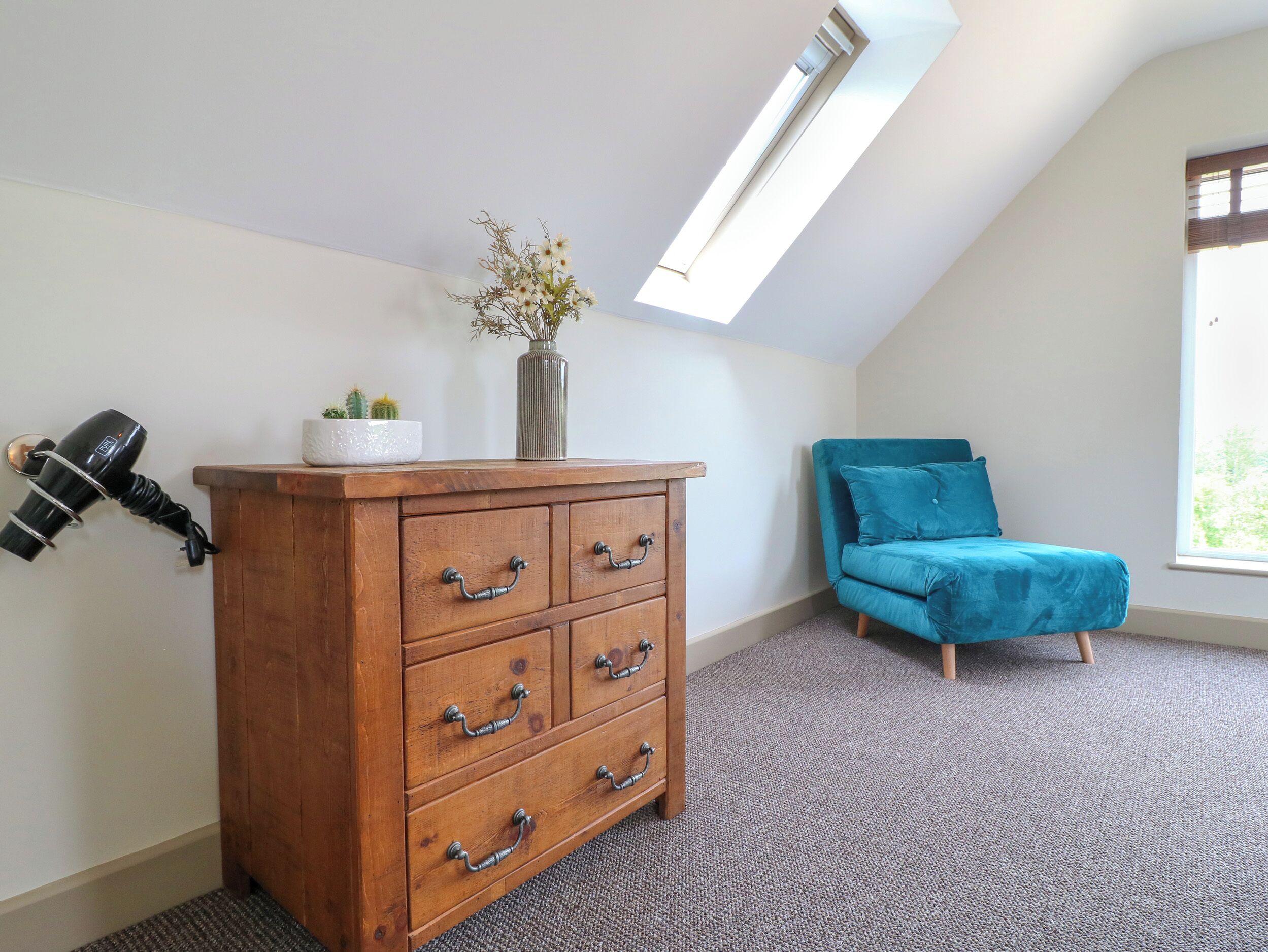 A room with a wooden dresser, a blue sofa, a skylight, and a window.